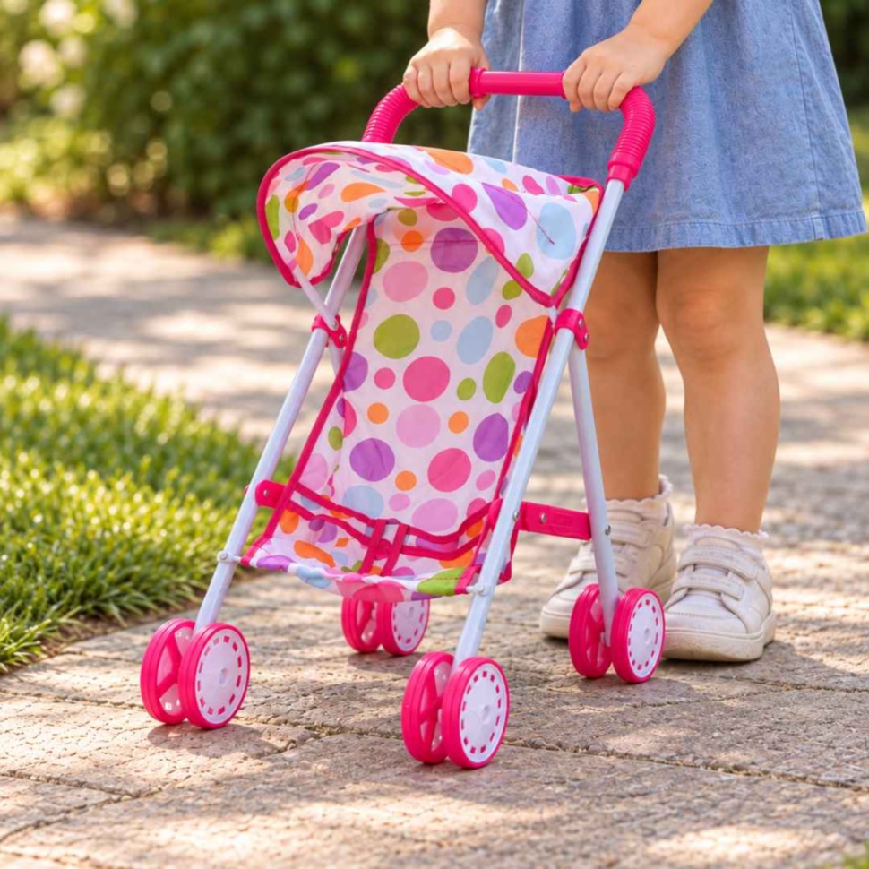 Copil plimbă căruciorul pentru păpuși cu mâner roz și buline colorate pe o alee